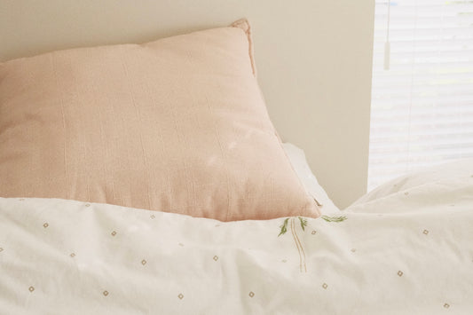 a bed with a white comforter and a pink pillow