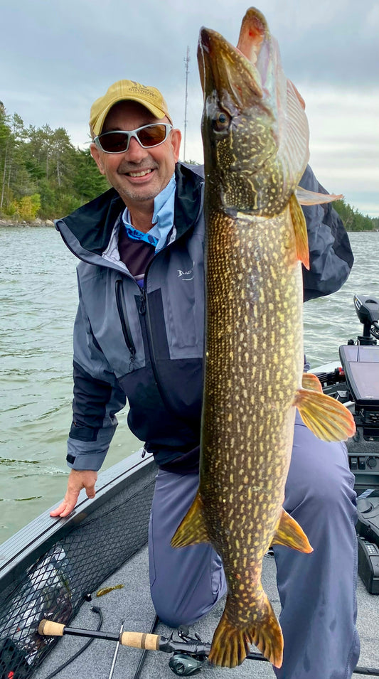 Man proudly holding a large pike fish on a boat